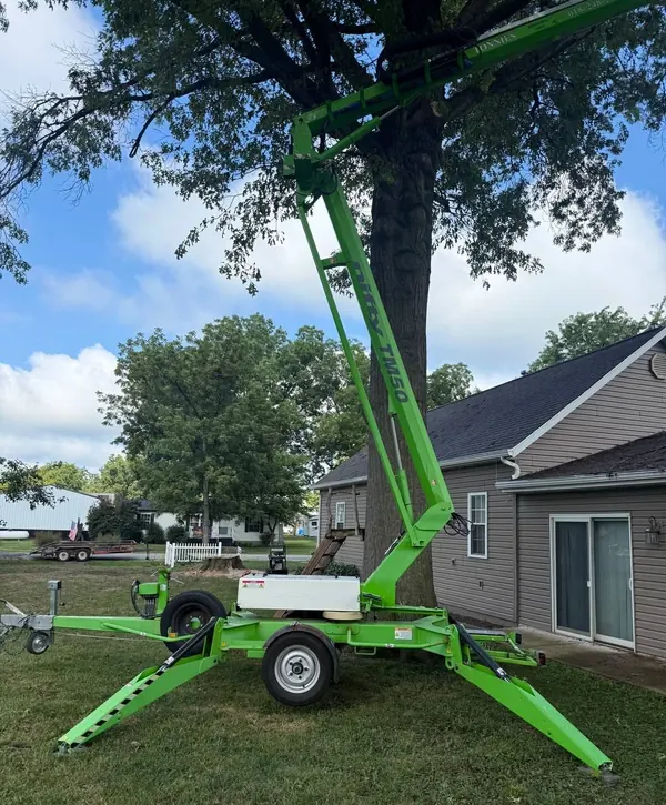 Towable boom lift set up on outriggers beside a large tree next to a house