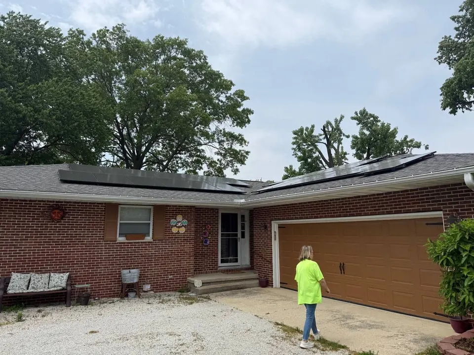 Mature trees growing close over a brick home roof with solar panels, the kind of clearance work we prune for
